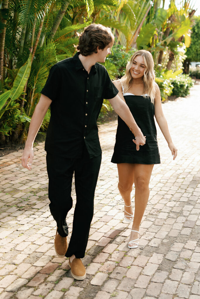 couple holding hands and walking at their downtown naples beach engagement session