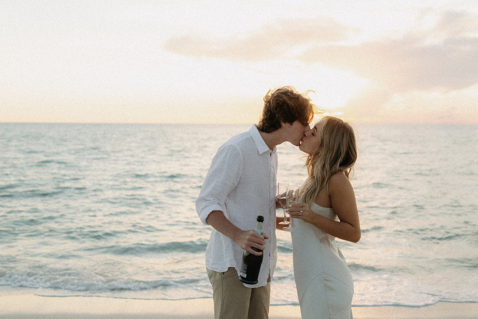 couple kissing and holding champagne in downtown naples beach for engagement photos