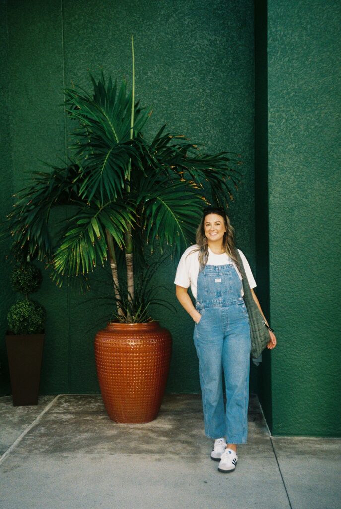 woman holding coffee posing in front of a floral painted wall to show things to do in naples florida