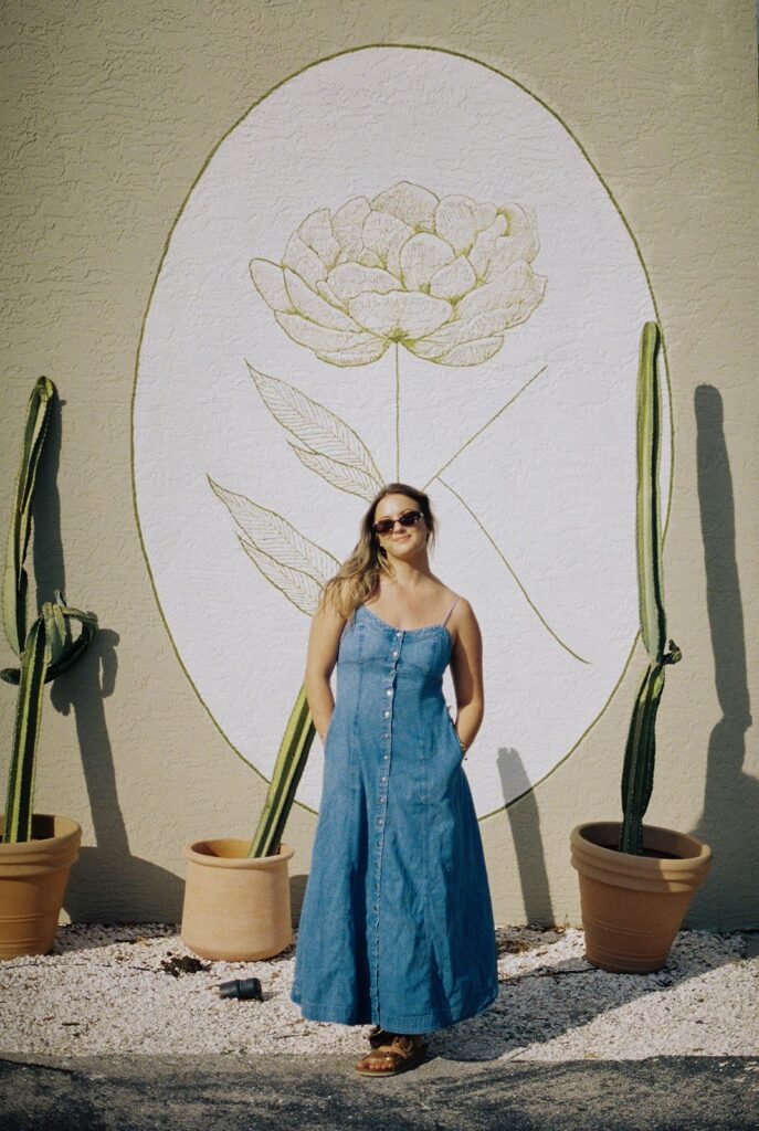 woman with hands in pockets posing in front of a floral painted wall to show things to do in naples florida